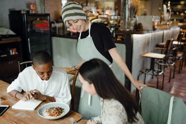 Restaurant scene with server in apron and customers dining, highlighting the importance of security guard services in hospitality