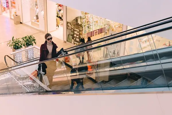 Modern shopping mall interior with escalator and shoppers, emphasizing the importance of security guard services in retail properties