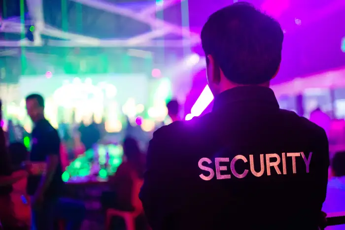 Security personnel in black jacket with 'SECURITY' monitoring lively event, highlighting industries security guard services in NYC