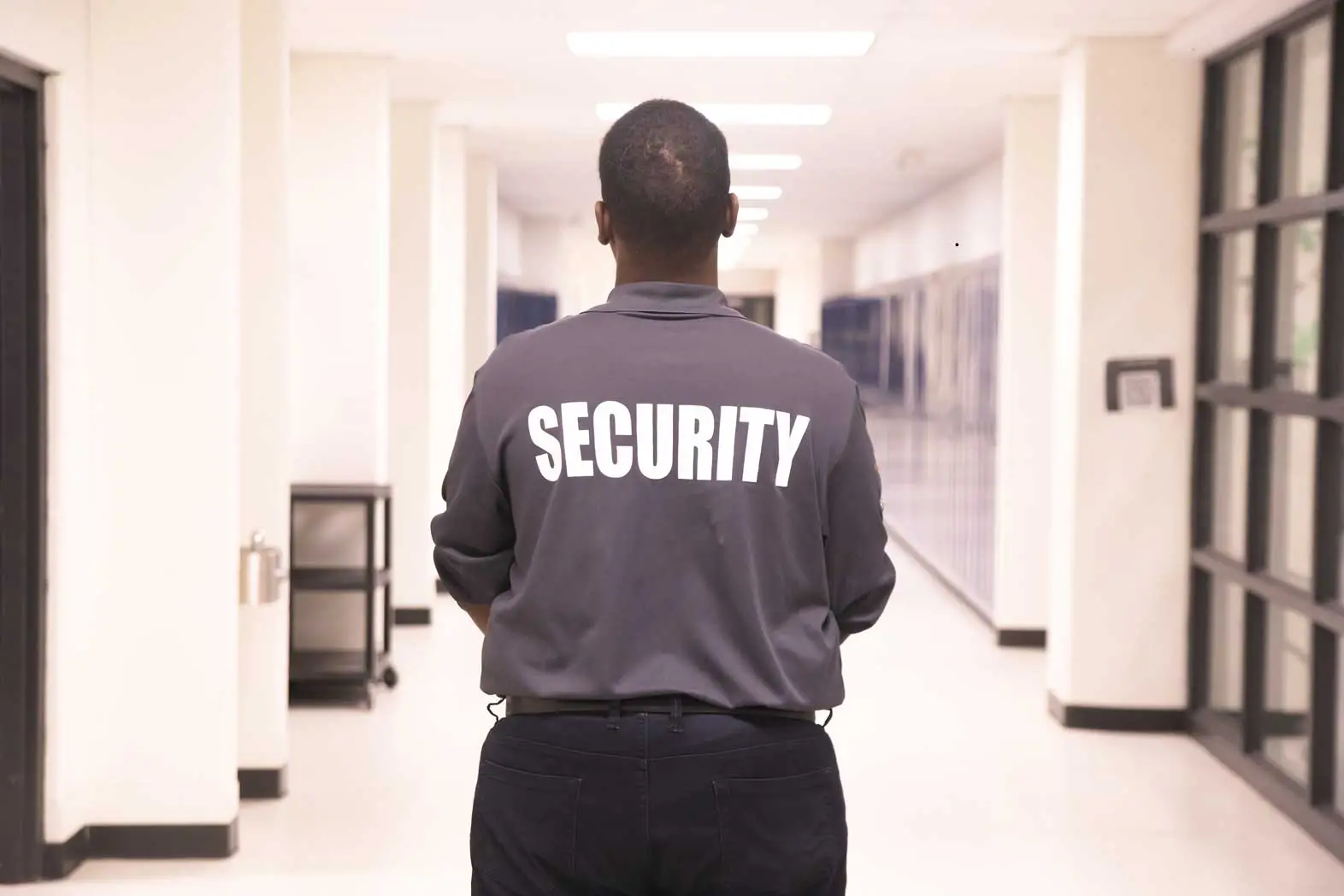 Security personnel in dark uniform with 'SECURITY' on back, monitoring hallway in institutional building, ensuring safety 