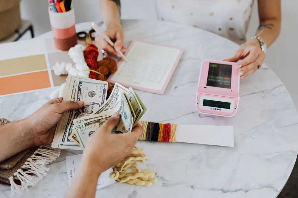 Two individuals counting cash and writing in notebook on white marble table, emphasizing the need for bank security guard