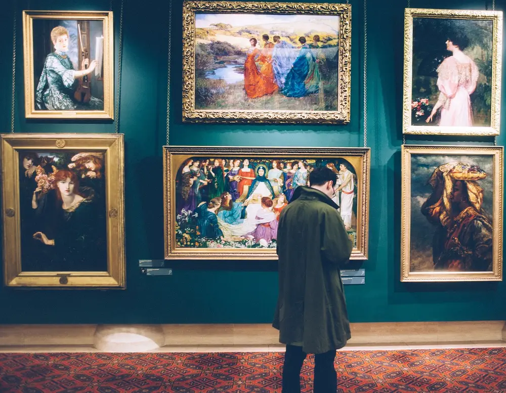 Individual observing framed paintings in art gallery, highlighting the importance of cultural property security guard services