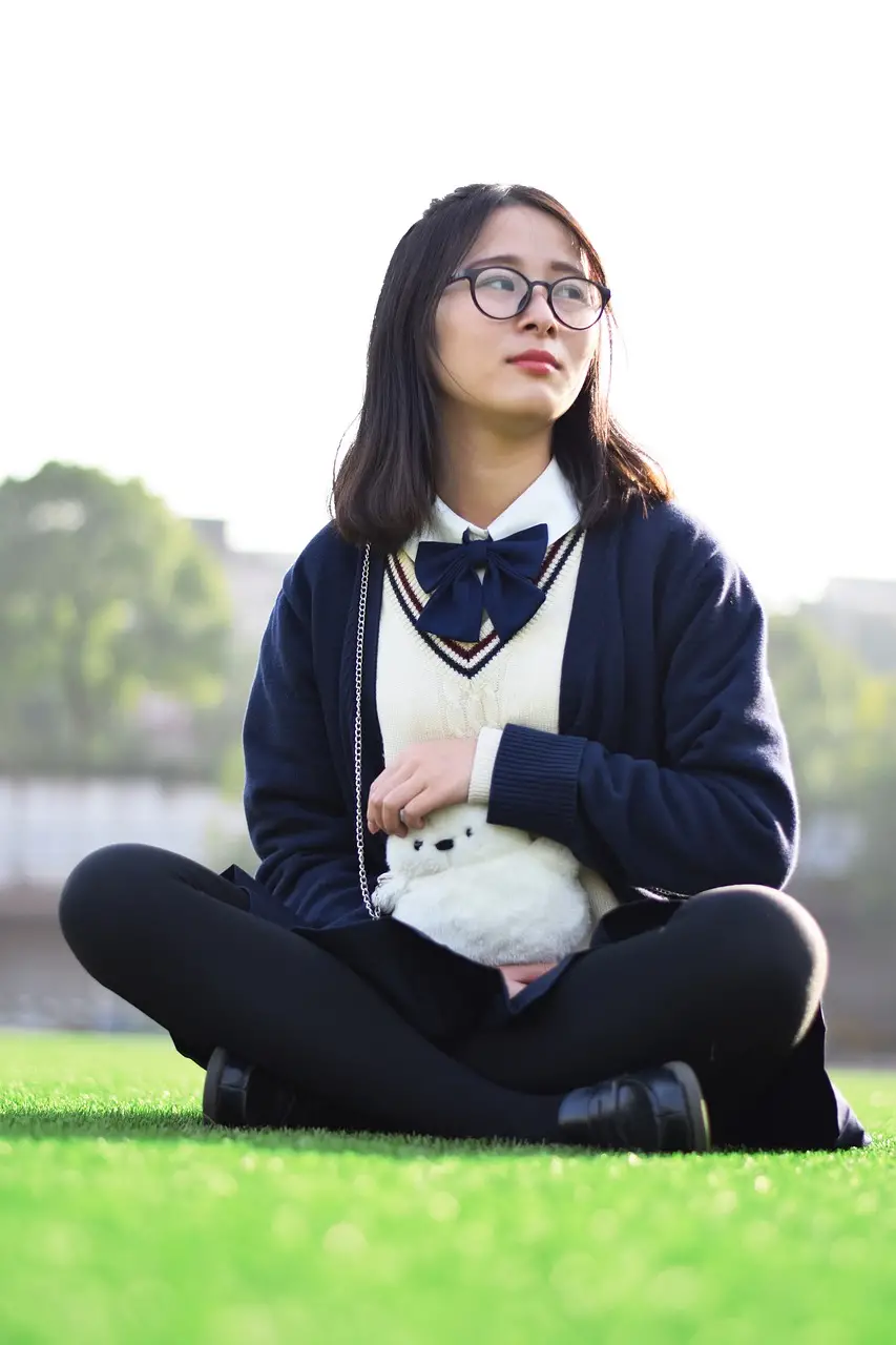 Student in school uniform sitting on grass with stuffed animal, highlighting the need for campus security guard services