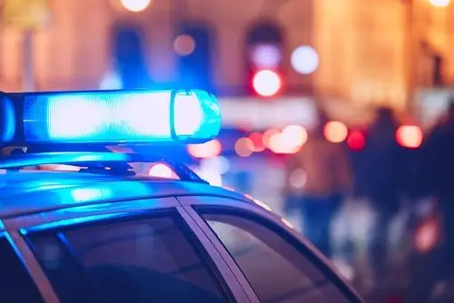 Close-up view of mobile patrol car with activated blue and white flashing lights parked on street at night, emphasizing security presence