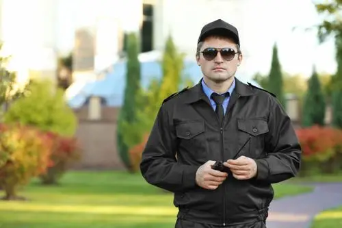 Professional security guard in black jacket and sunglasses standing in green park, exuding vigilance and style in outdoor setting